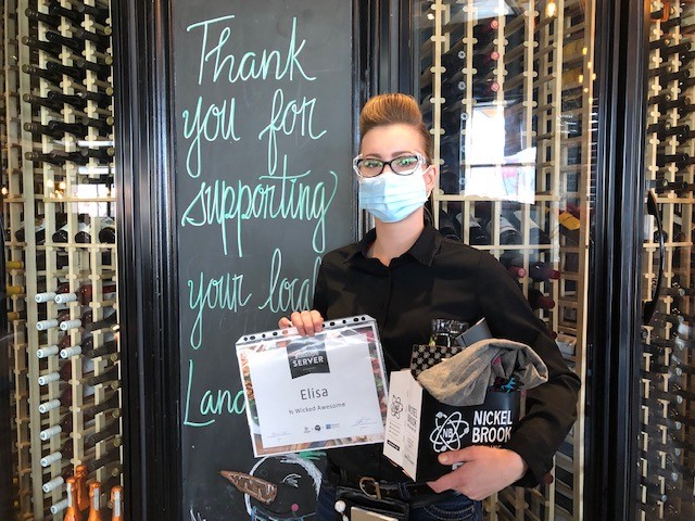 Photo of Elisa the server standing holding a certificate and Nickelbrook prize pack, she is wearing a mask