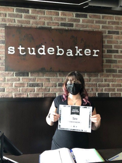 Female winner standing in front of studebaker sign with glasses and black mask holding winning certificate